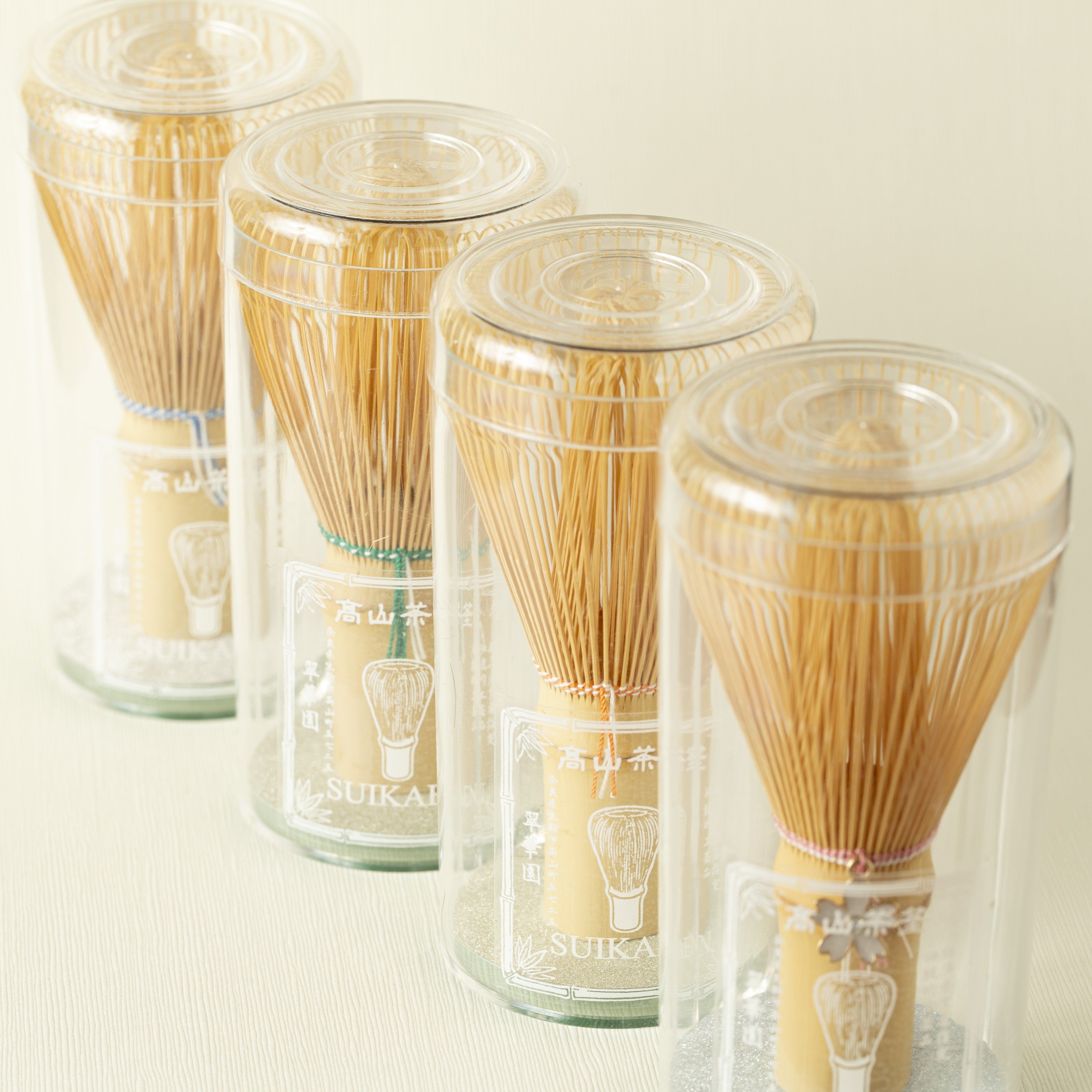 Set of four bamboo whisk - chasen - tools in clear plastic containers on a light background