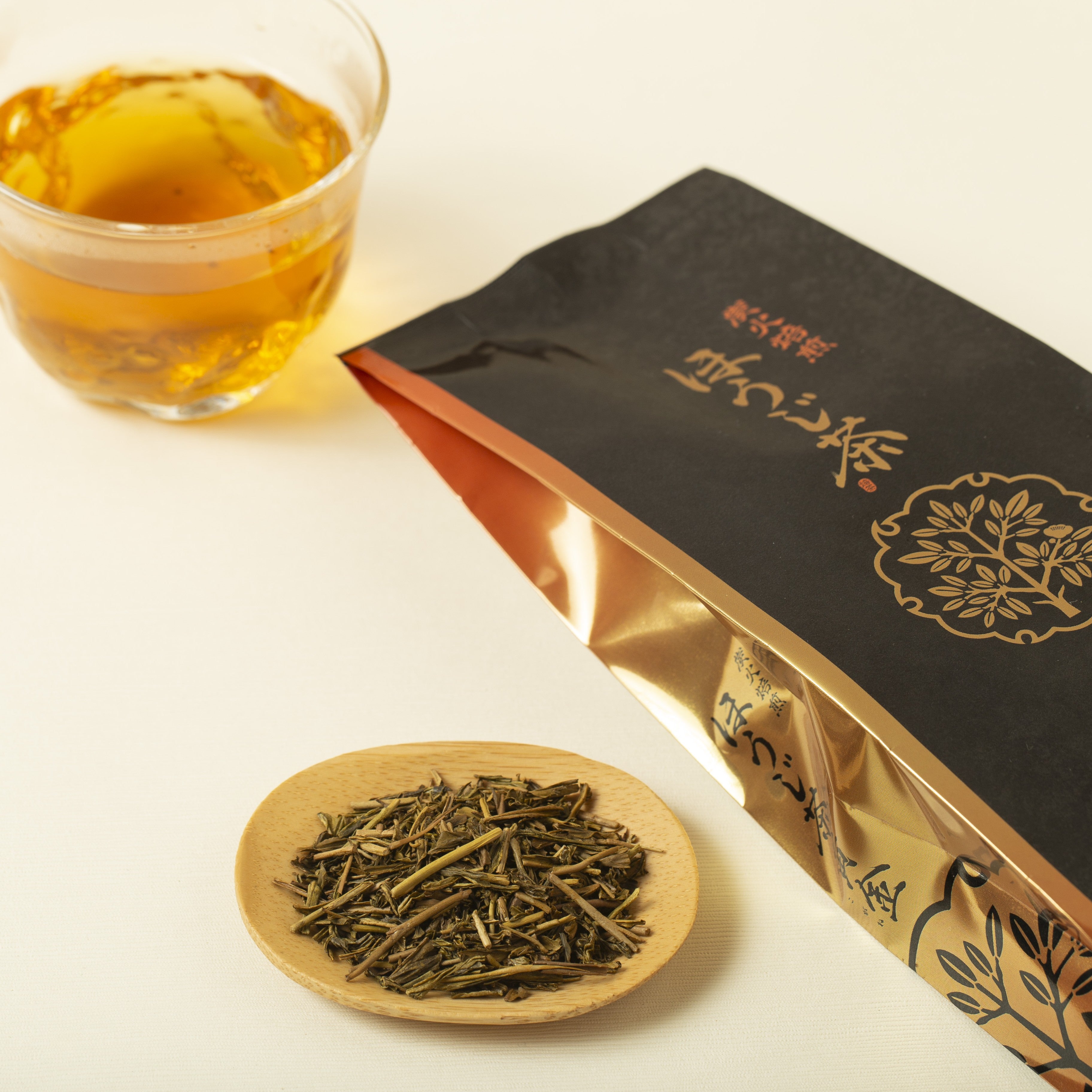 Hojicha packaging with a glass of tea and a bowl of tea leaves on a white background