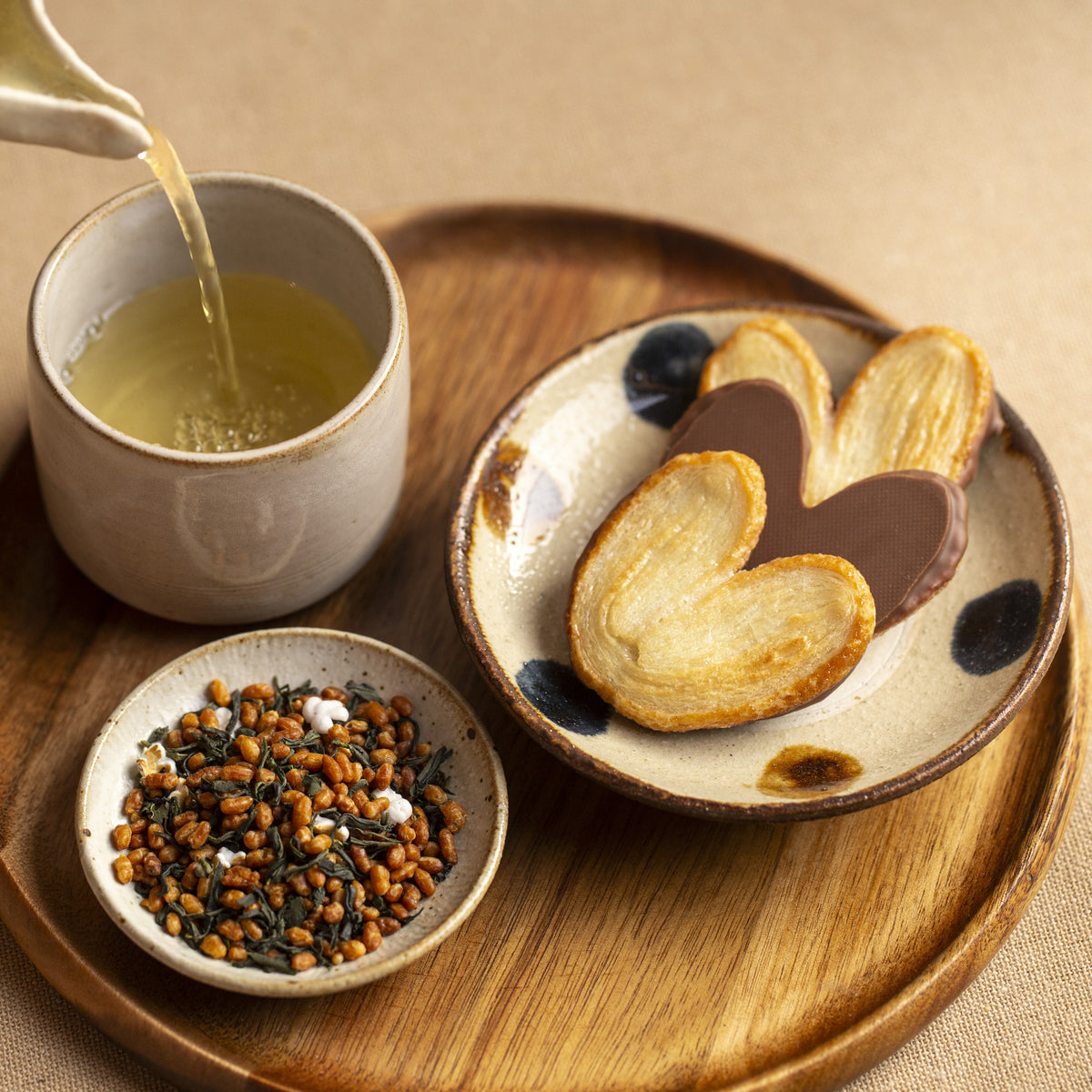 Tea being poured into a cup with a side of cookies and tea leaves on a wooden tray.