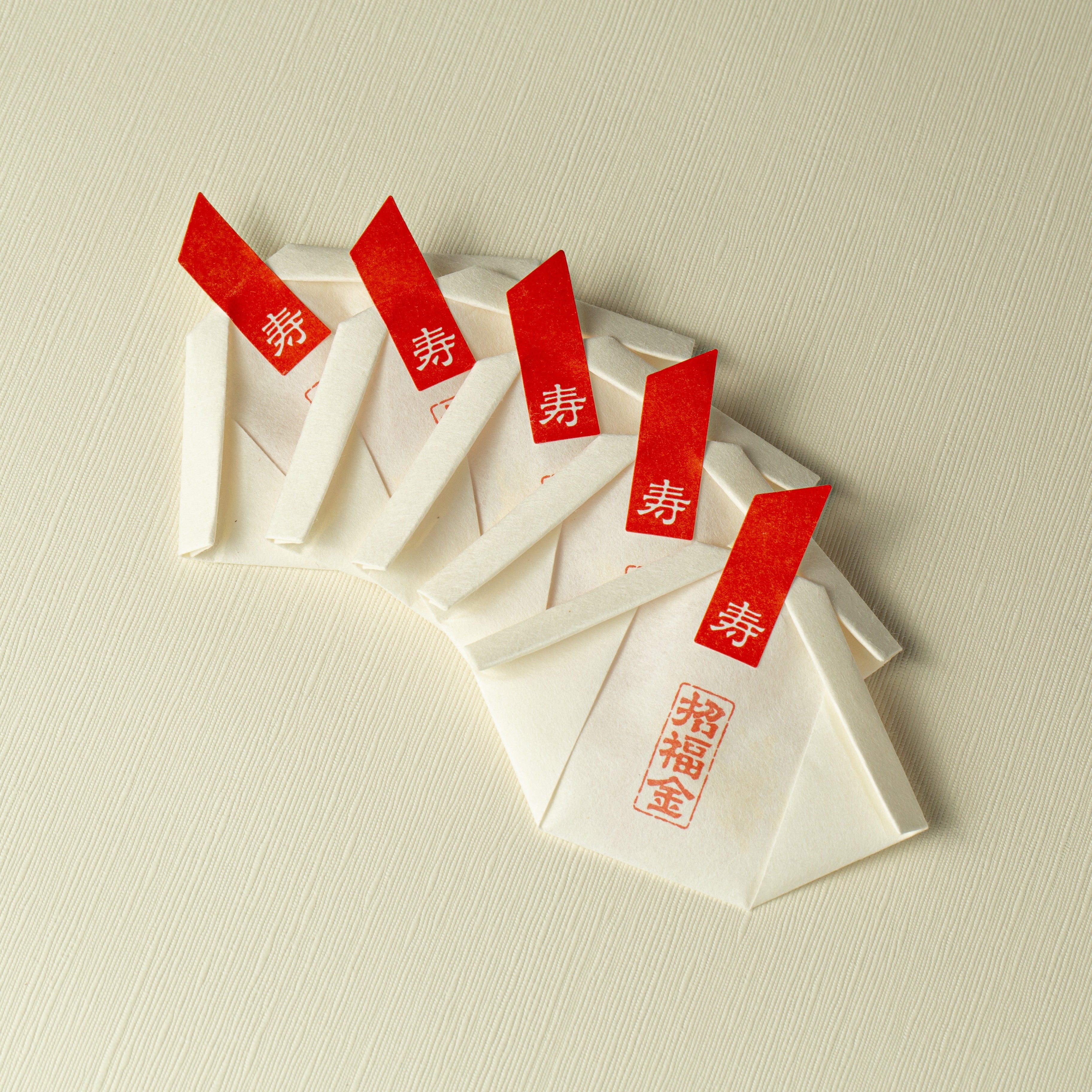 White envelopes with red labels containing gold edible gold glitter flakes on a beige background