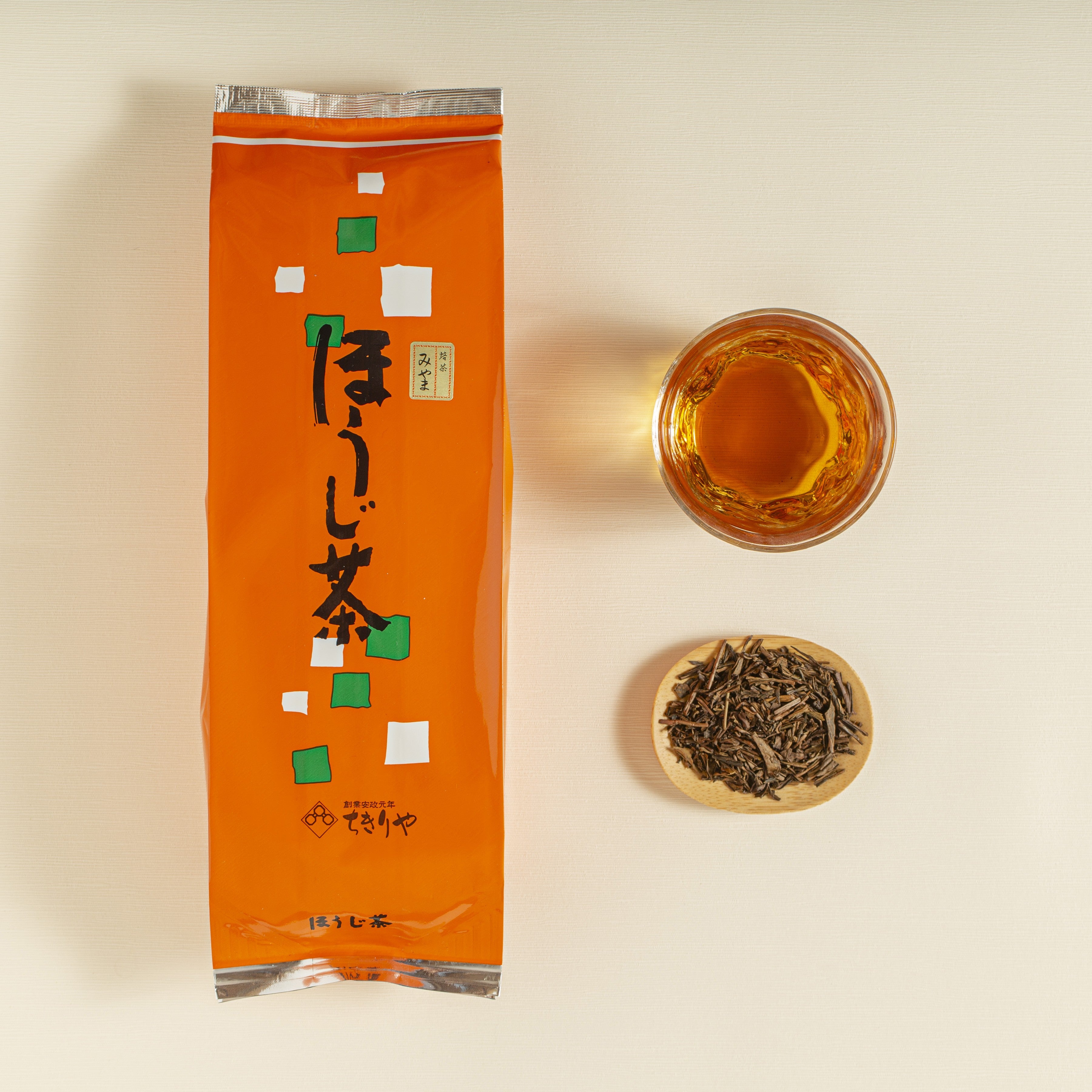 Orange tea package with a glass of tea and a bowl of loose tea leaves on a beige background