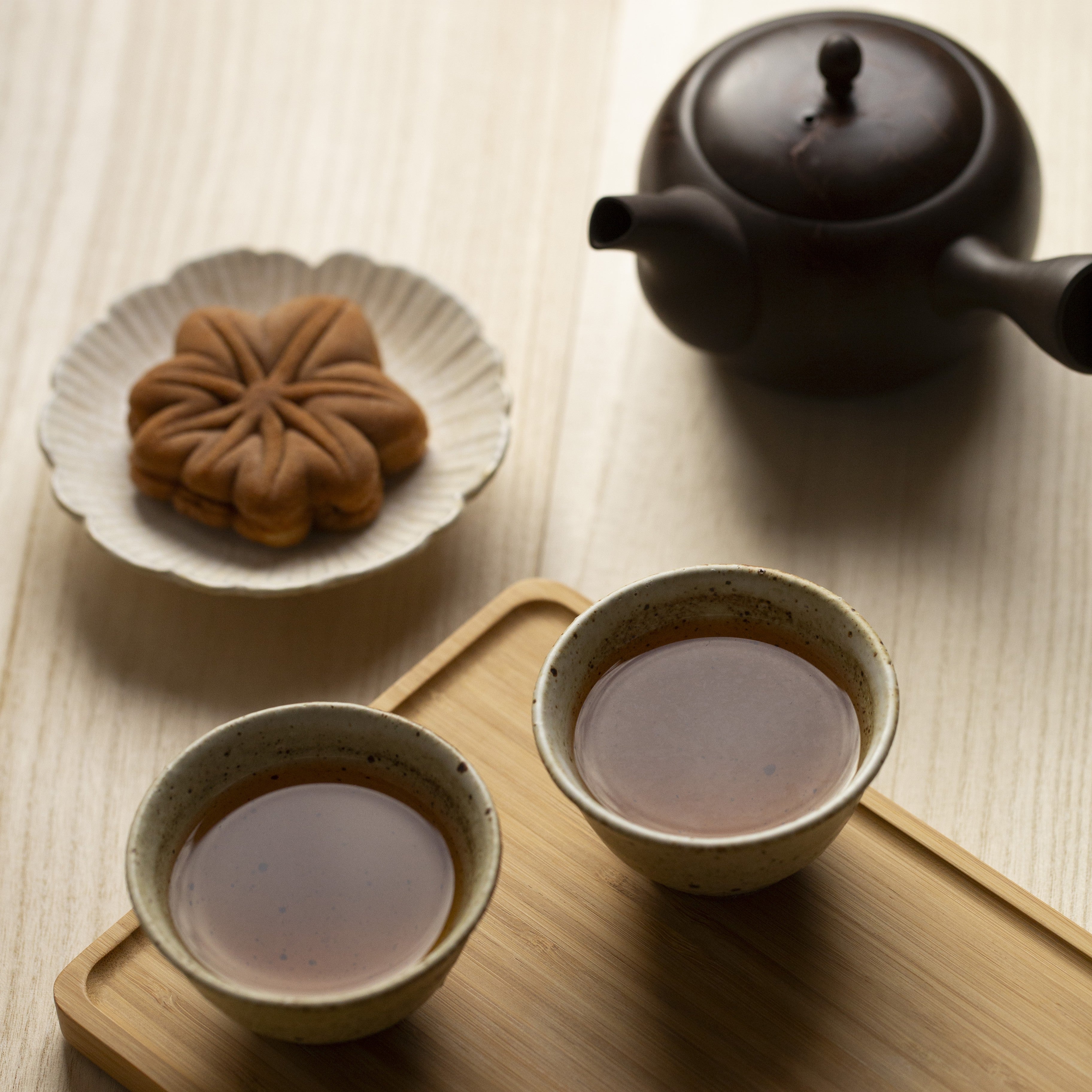 Tea set with two cups, a teapot, and a plate with a pastry on a wooden tray.