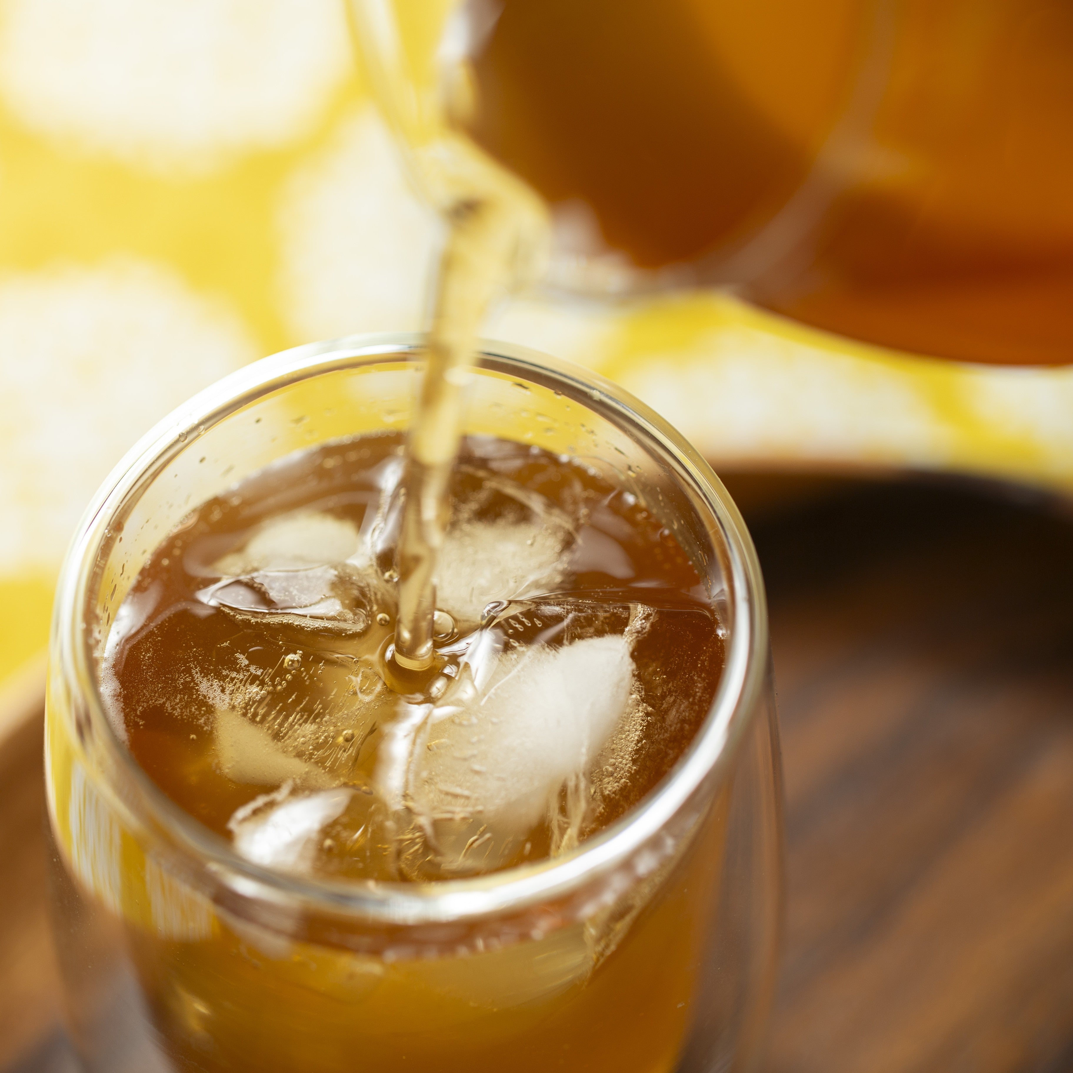 Kuromame tea being poured into a glass with ice cubes on a wooden surface.