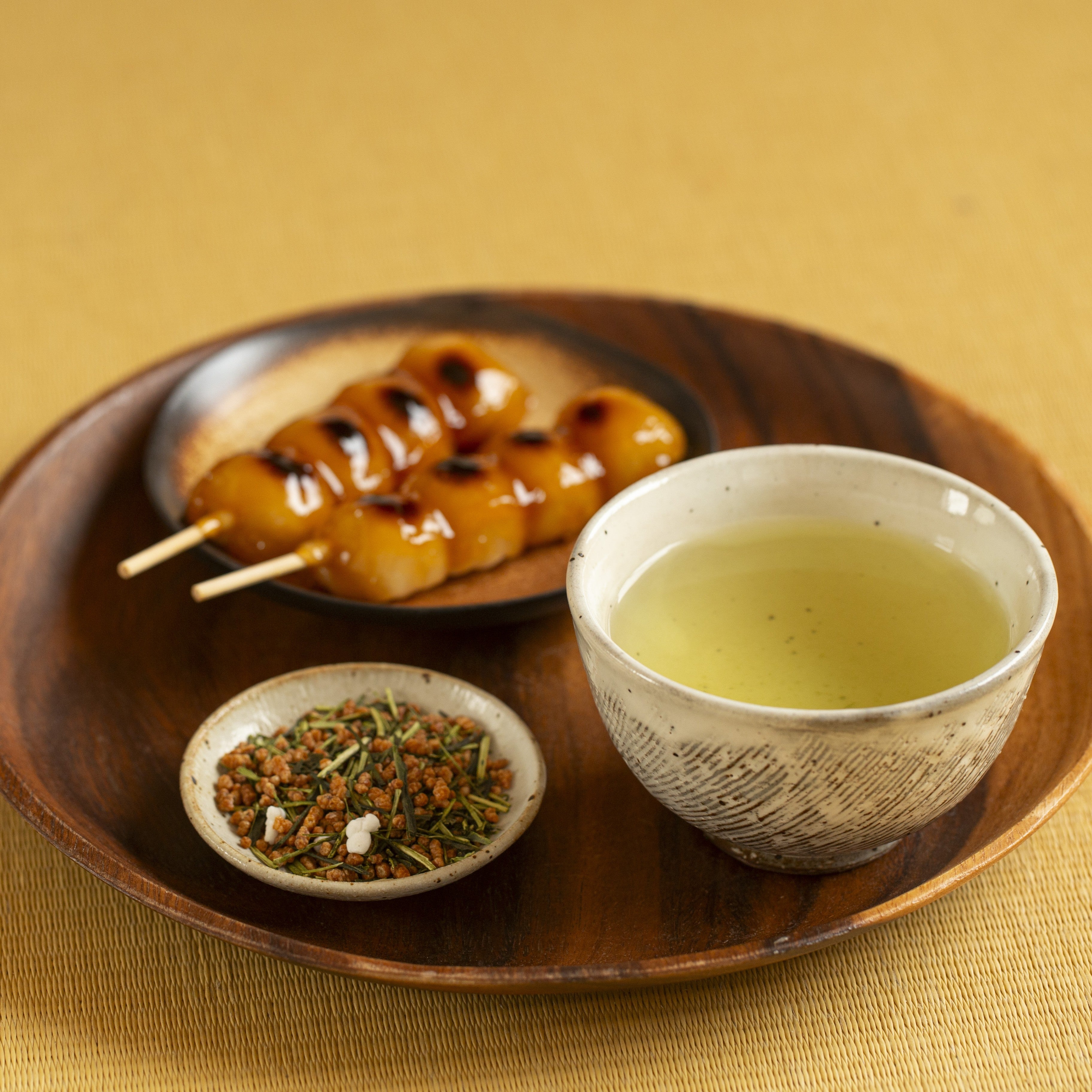 Tea cup with green tea, tea leaves and a small dish of dango on a wooden tray.