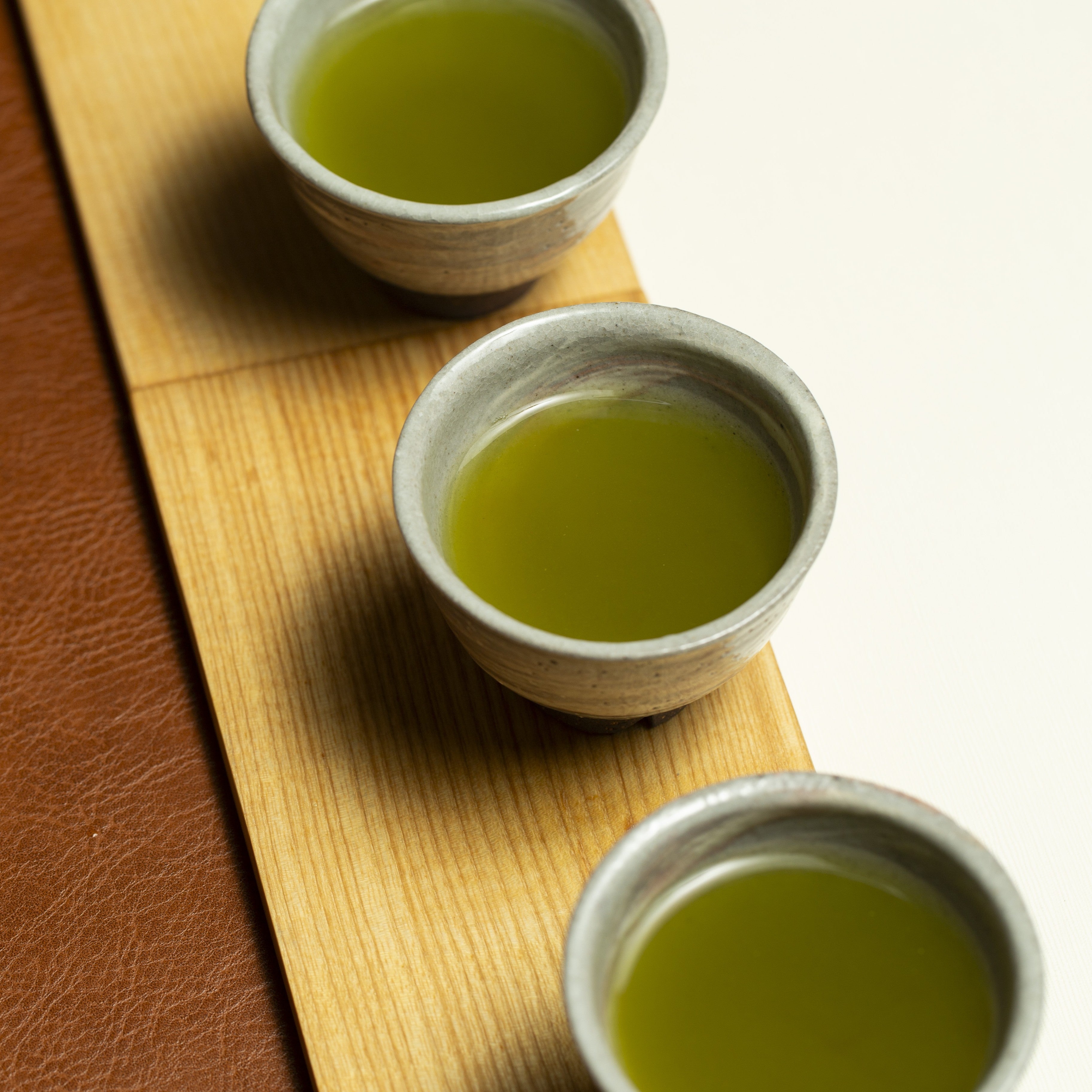 Three ceramic cups filled with green tea - Kyoto Fukamushi Sencha - on a wooden surface.