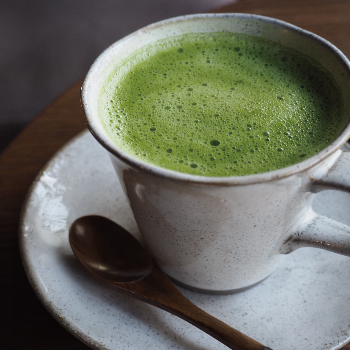 Cup of green tea with a green tea package on a wooden surface.