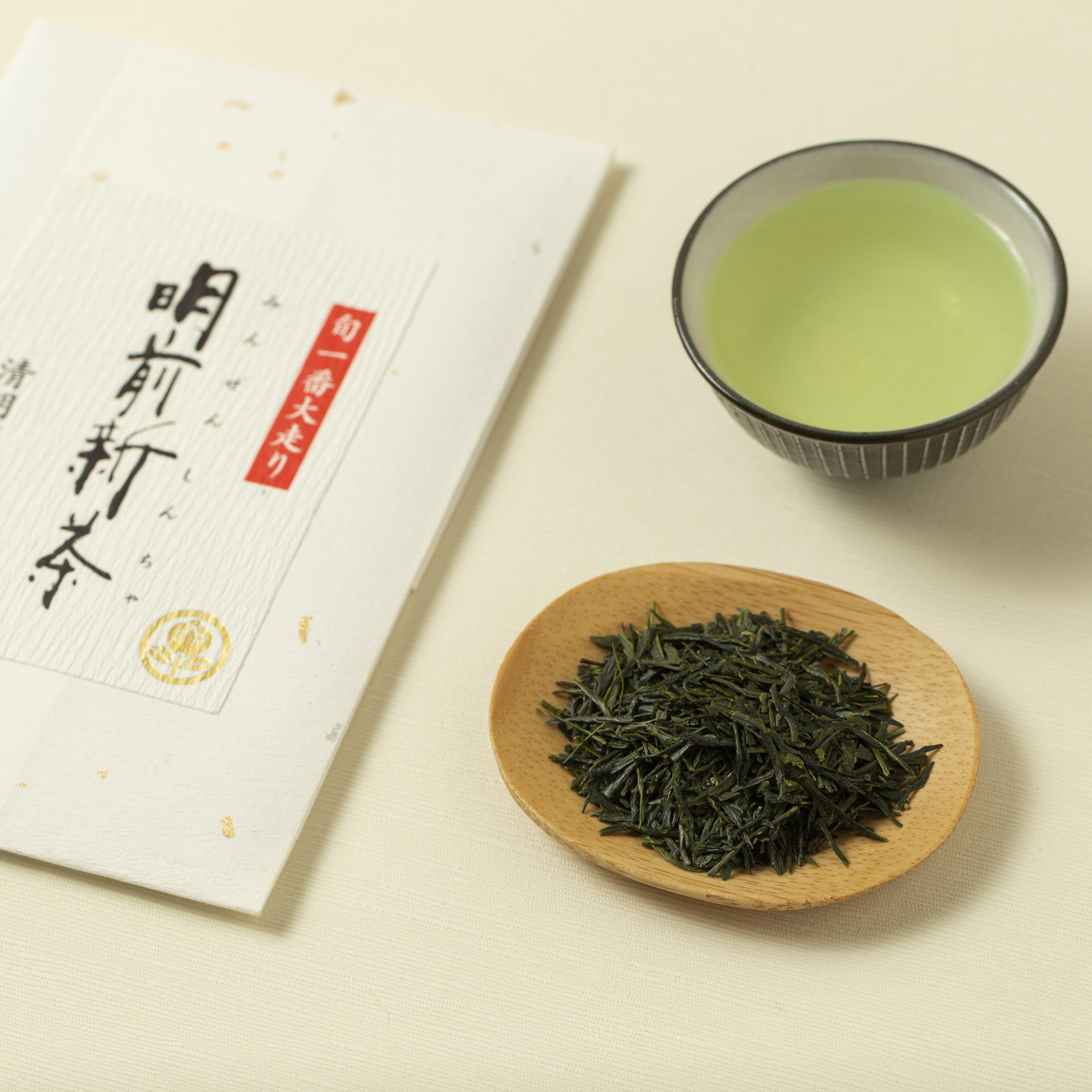 Green tea leaves on a wooden dish with a cup of green tea and a tea package on a light background
