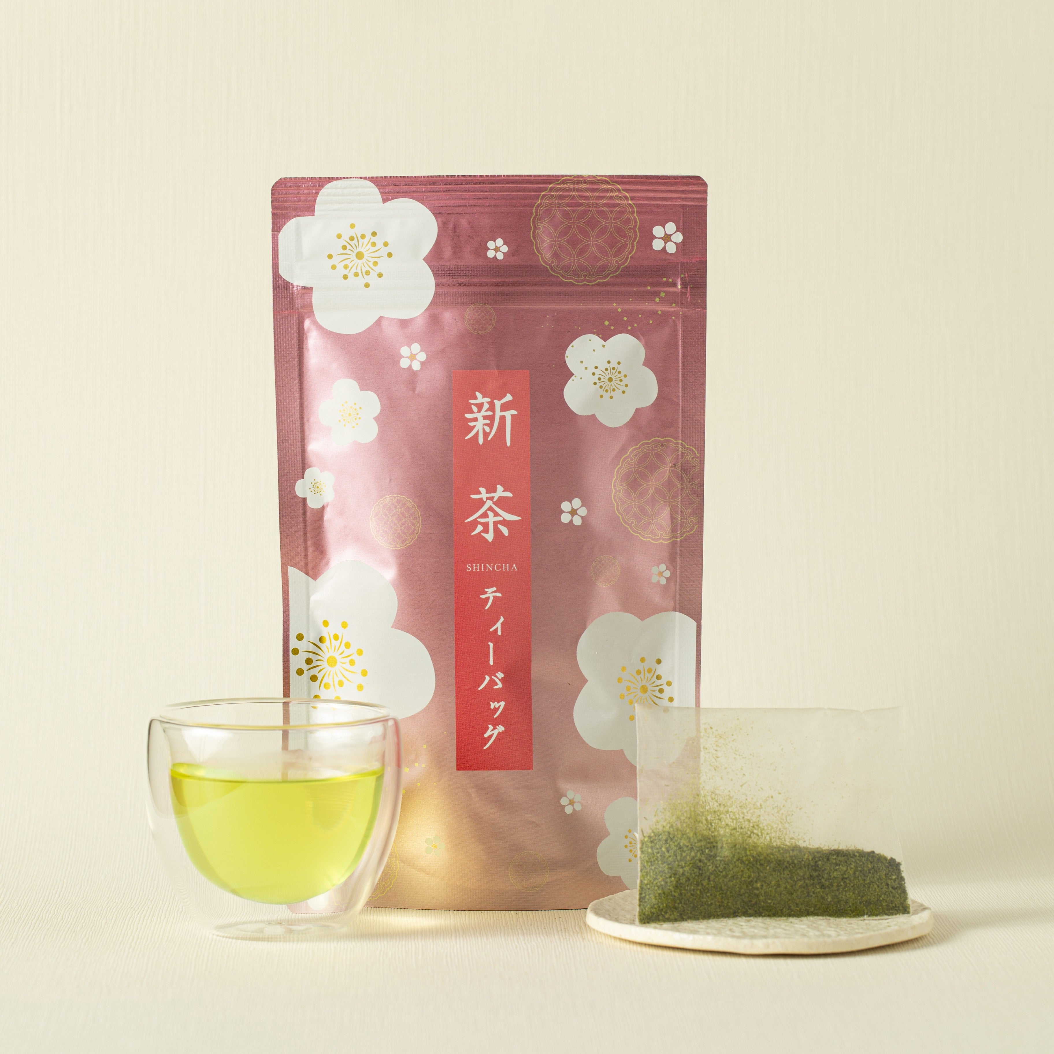 Tea package with floral design, glass of green tea, and tea bag on a light background