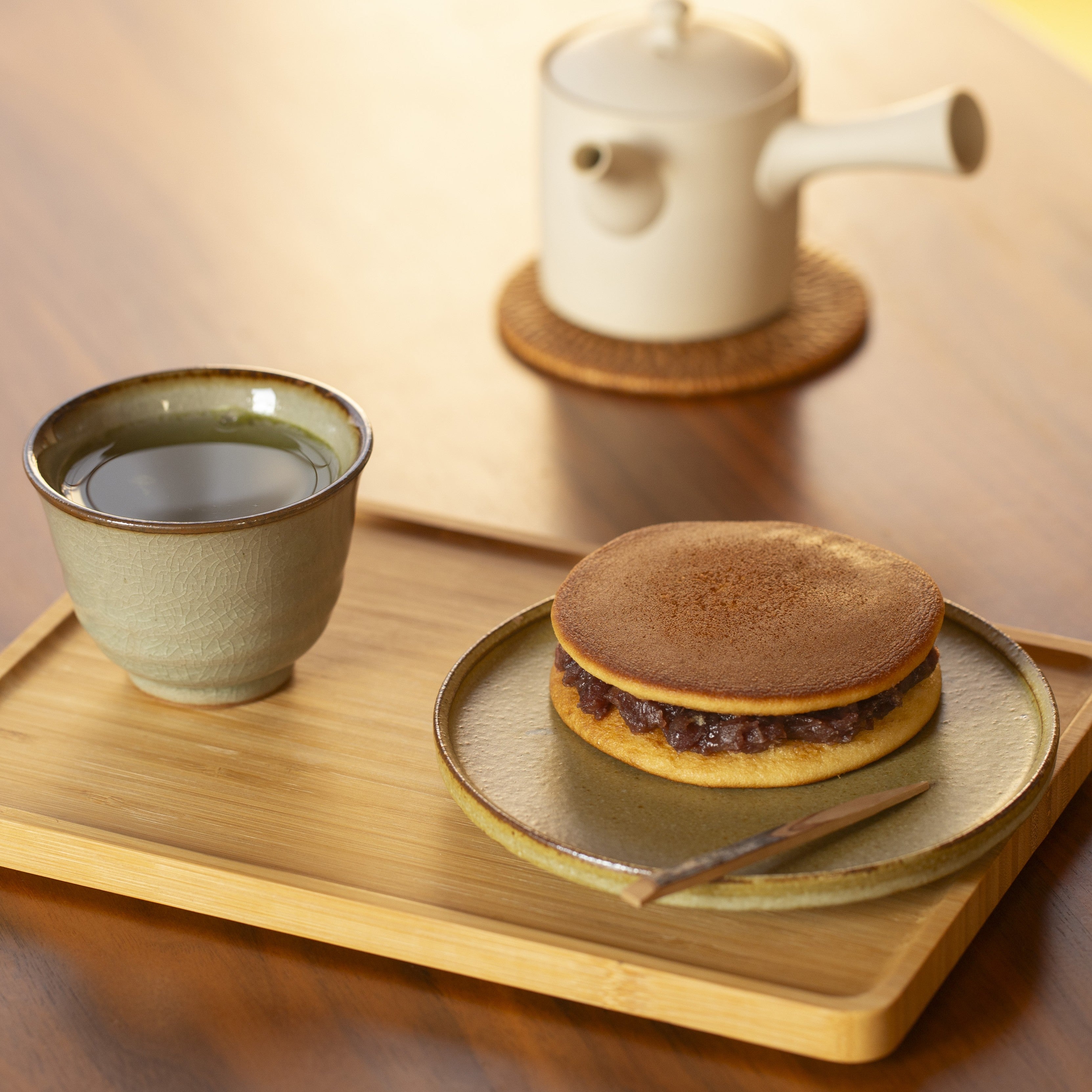 Tea cup and dorayaki on a wooden tray with a teapot in the background