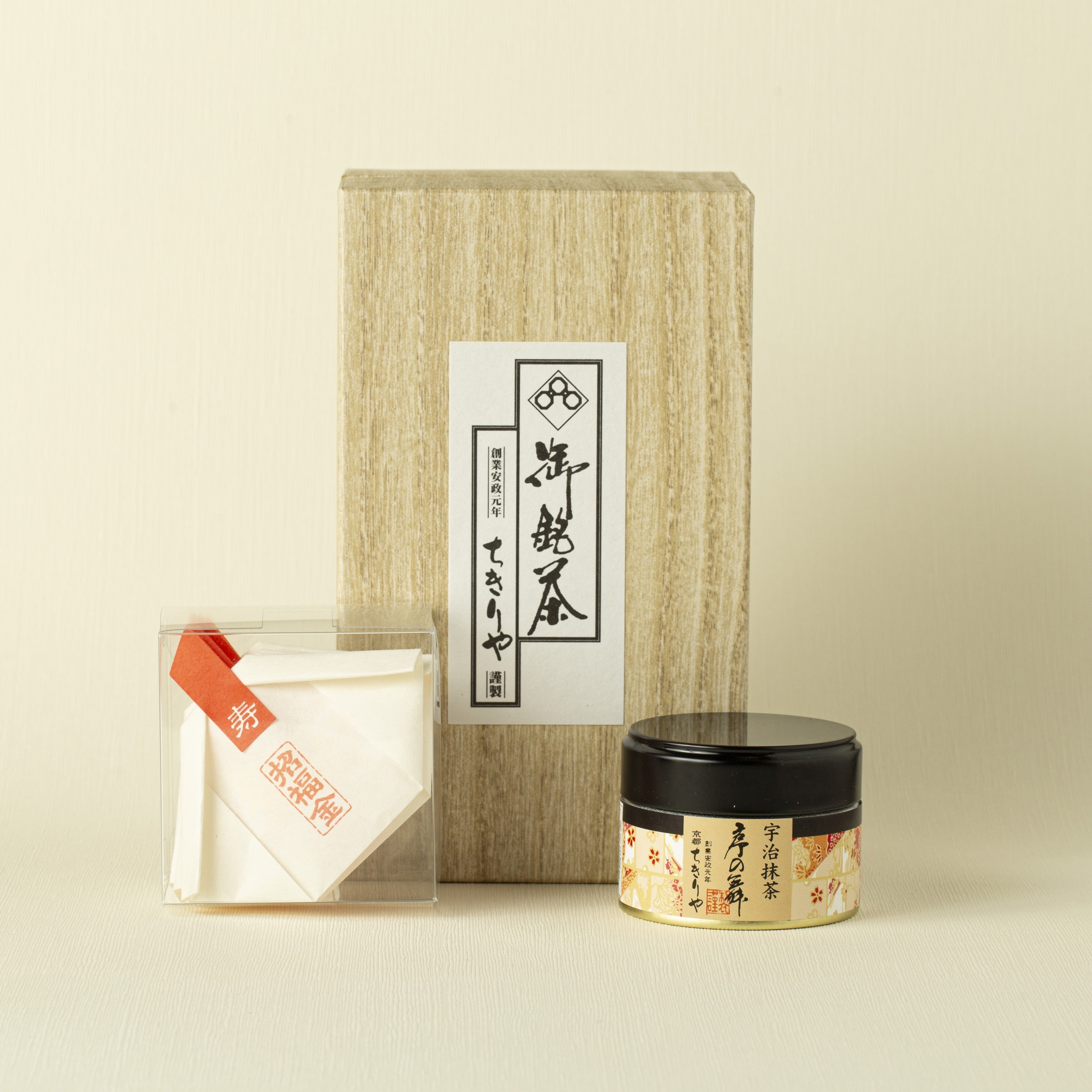 Tea packaging set with a wooden box, transparent container with gold glitter flakes, and small jar can of matcha on a beige background
