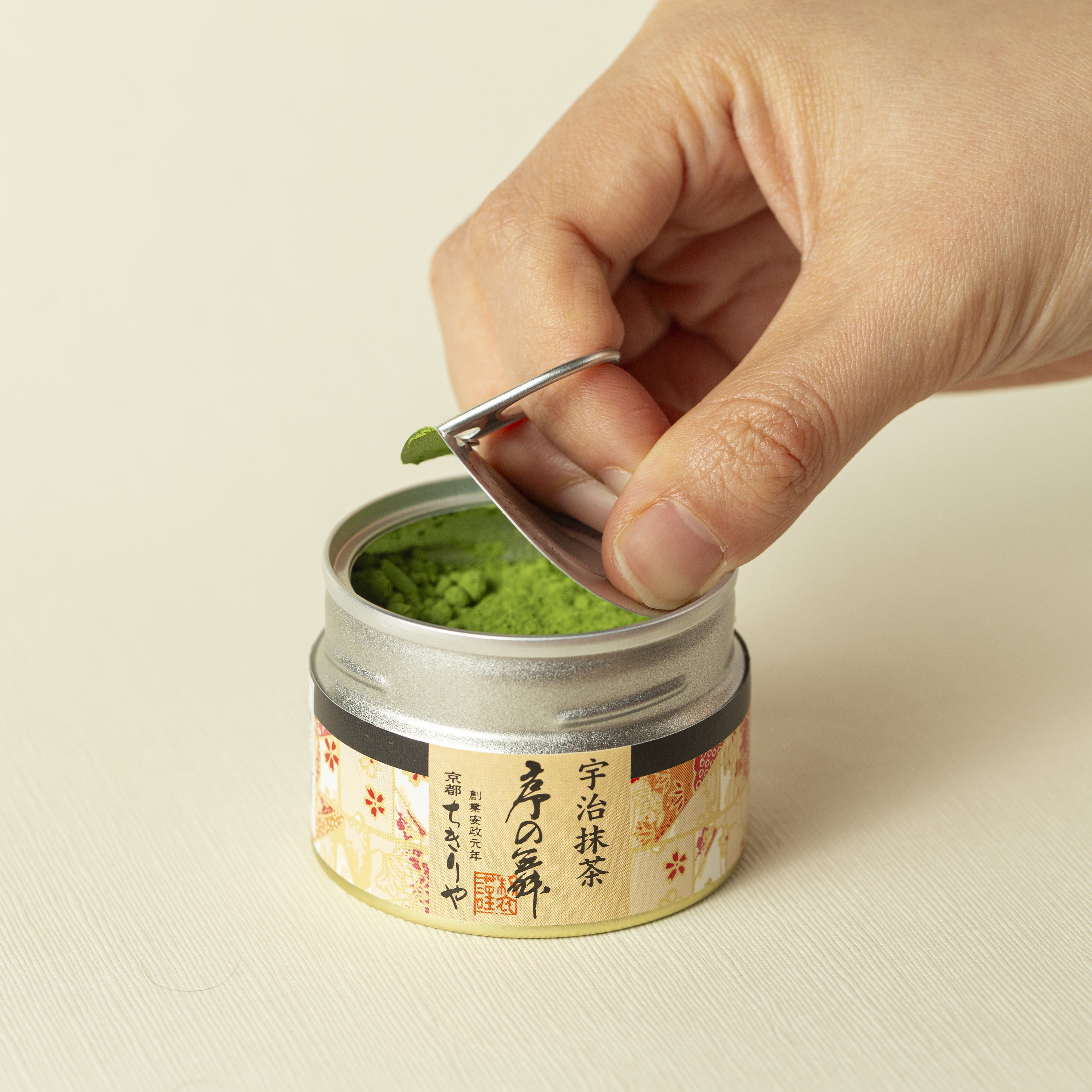 Hand scooping matcha green tea powder from a small metal container.