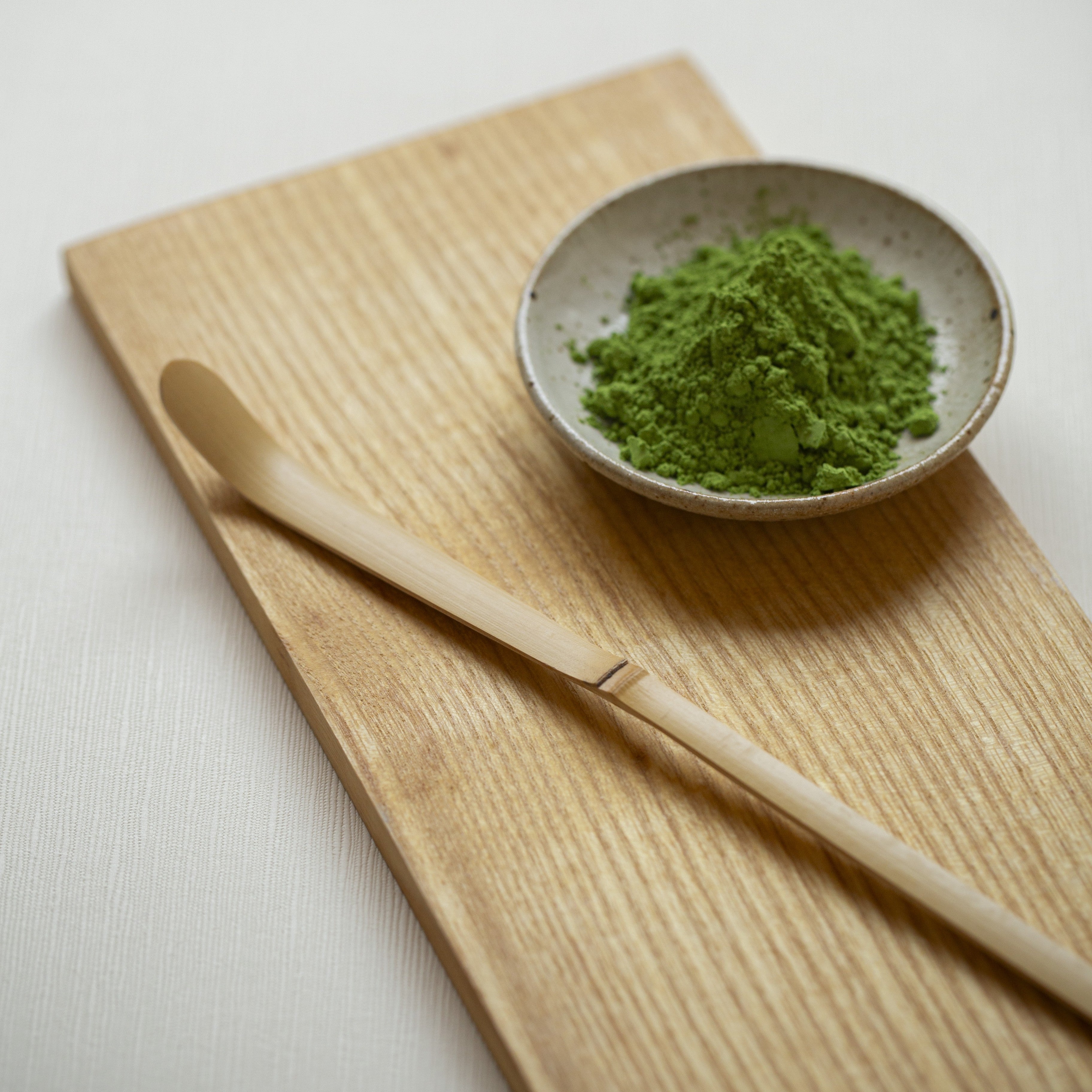 Matcha green tea powder in a small bowl on a wooden board with a wooden spoon.