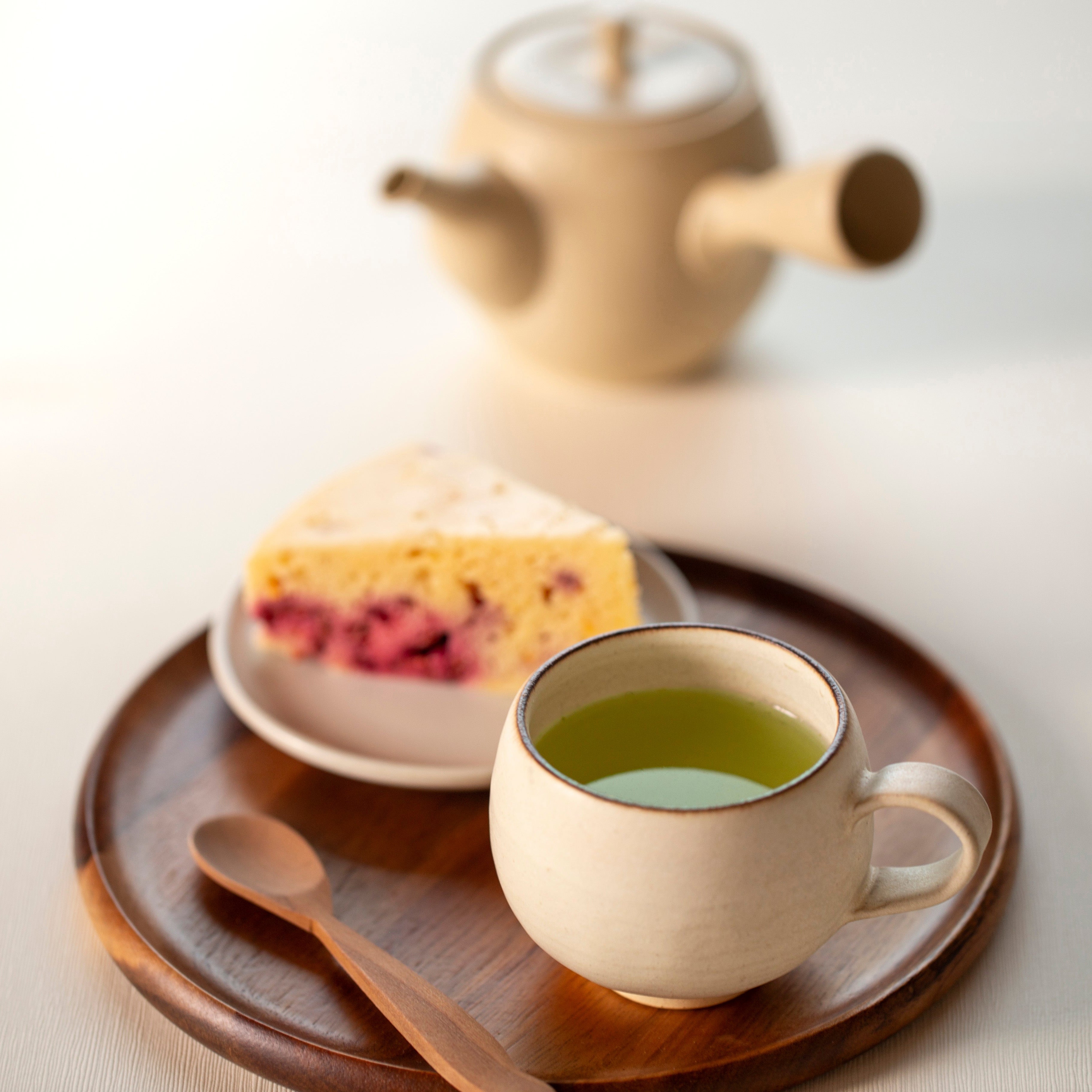 Japanese green tea cup with green tea, cake, and teapot on a wooden tray.
