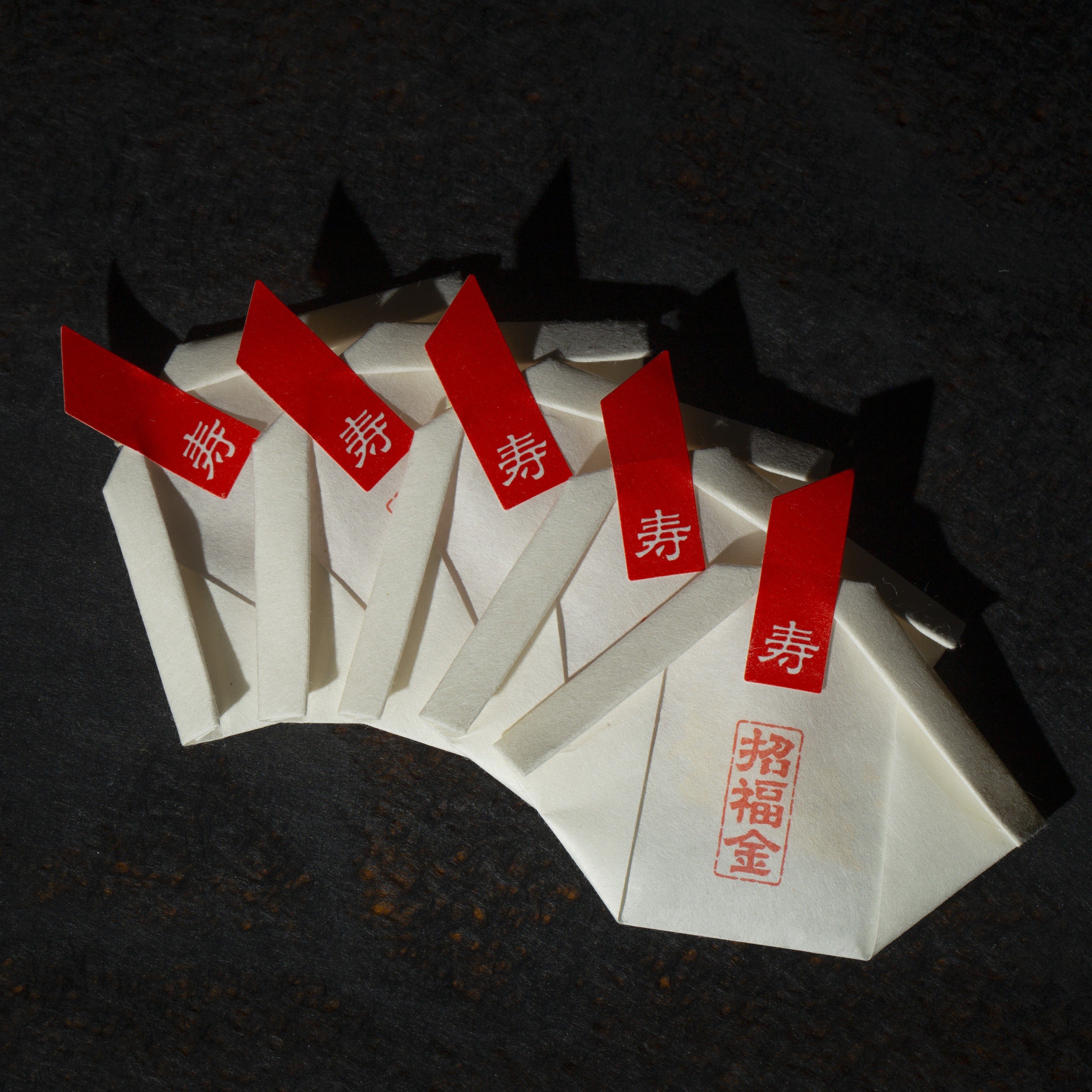 White envelopes with red labels containing gold edible gold glitter flakes on a dark background