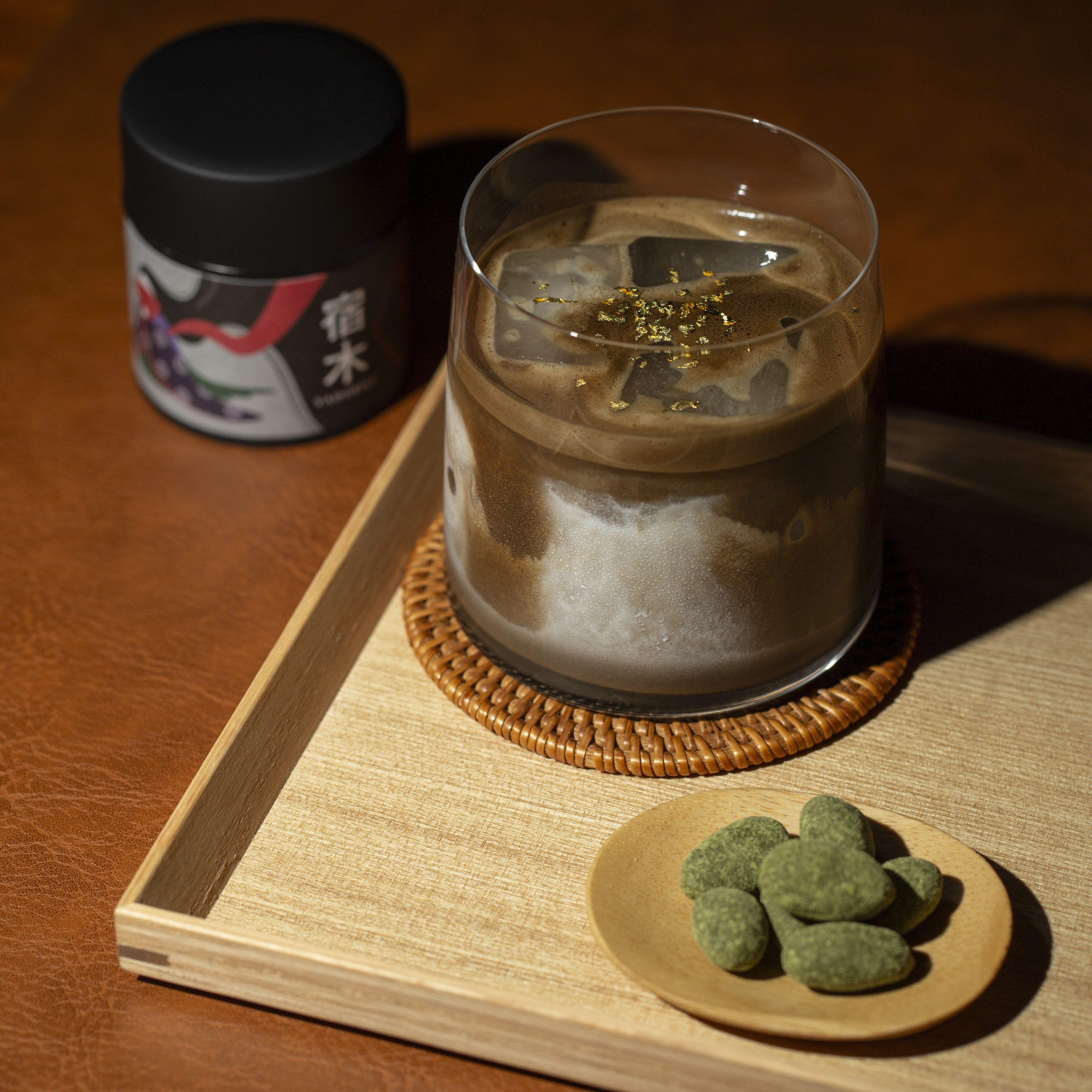 Glass of hojicha latte on a wooden tray, matcha almonds and hojicha yadorigi can.
