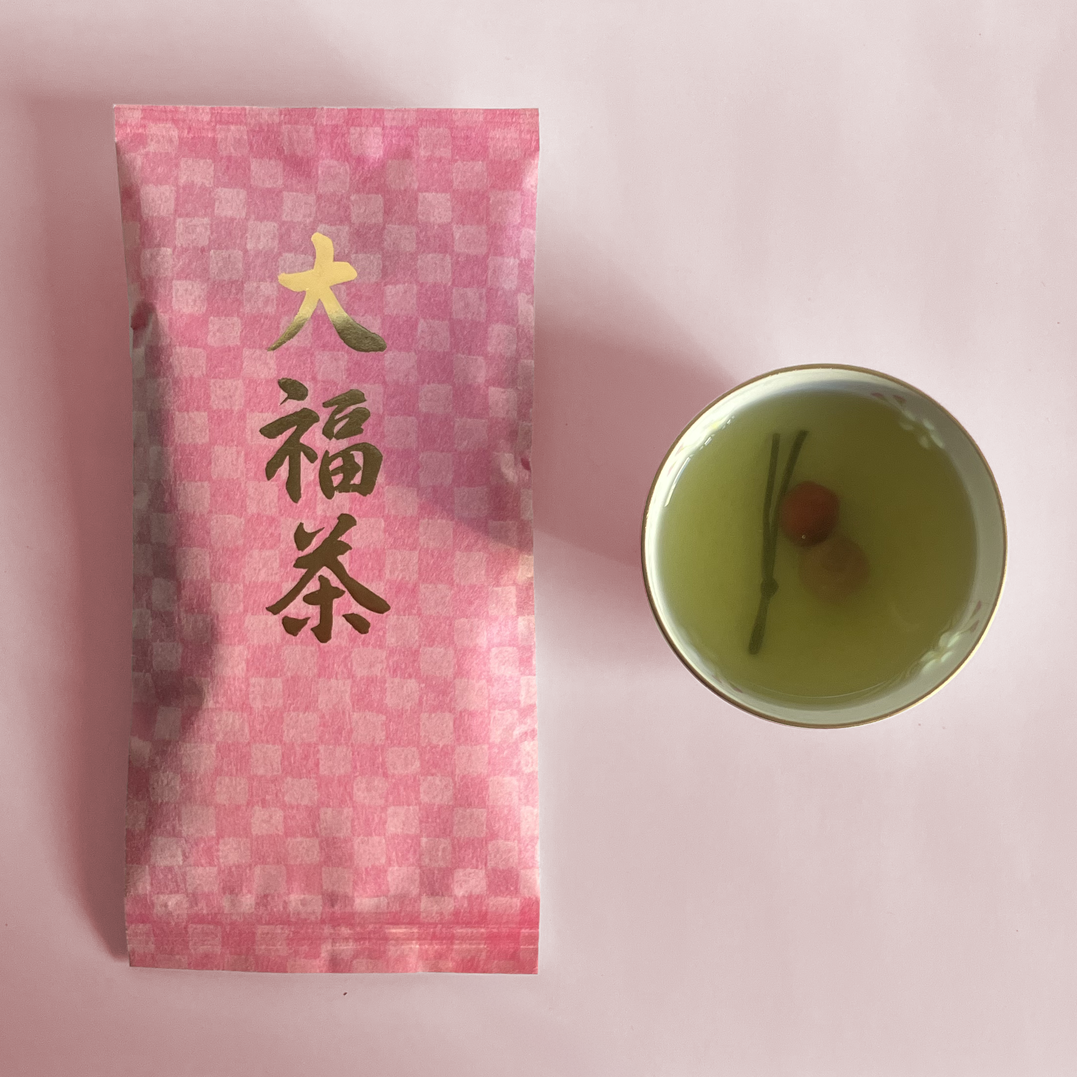 Pink tea package with gold text next to a small cup of green tea
