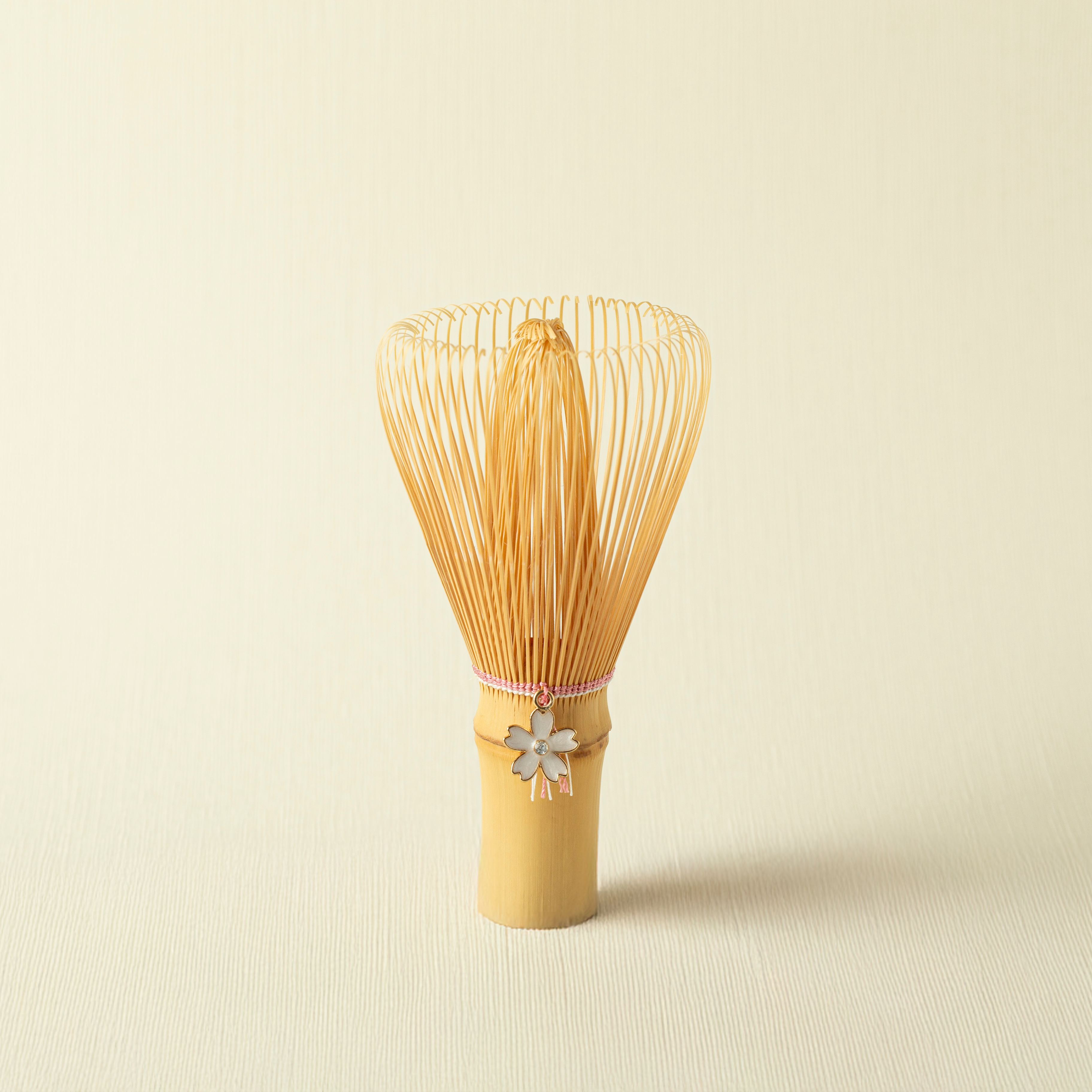 Bamboo whisk - chasen - with a decorative sakura cherry blossom charm on a beige background