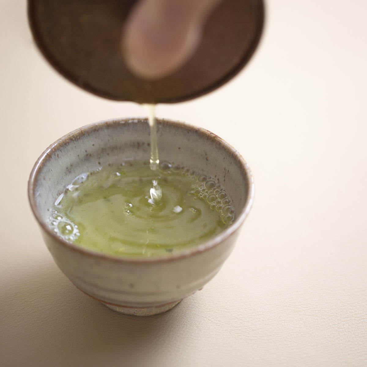 Green tea sencha yame being poured into a ceramic cup on a light surface
