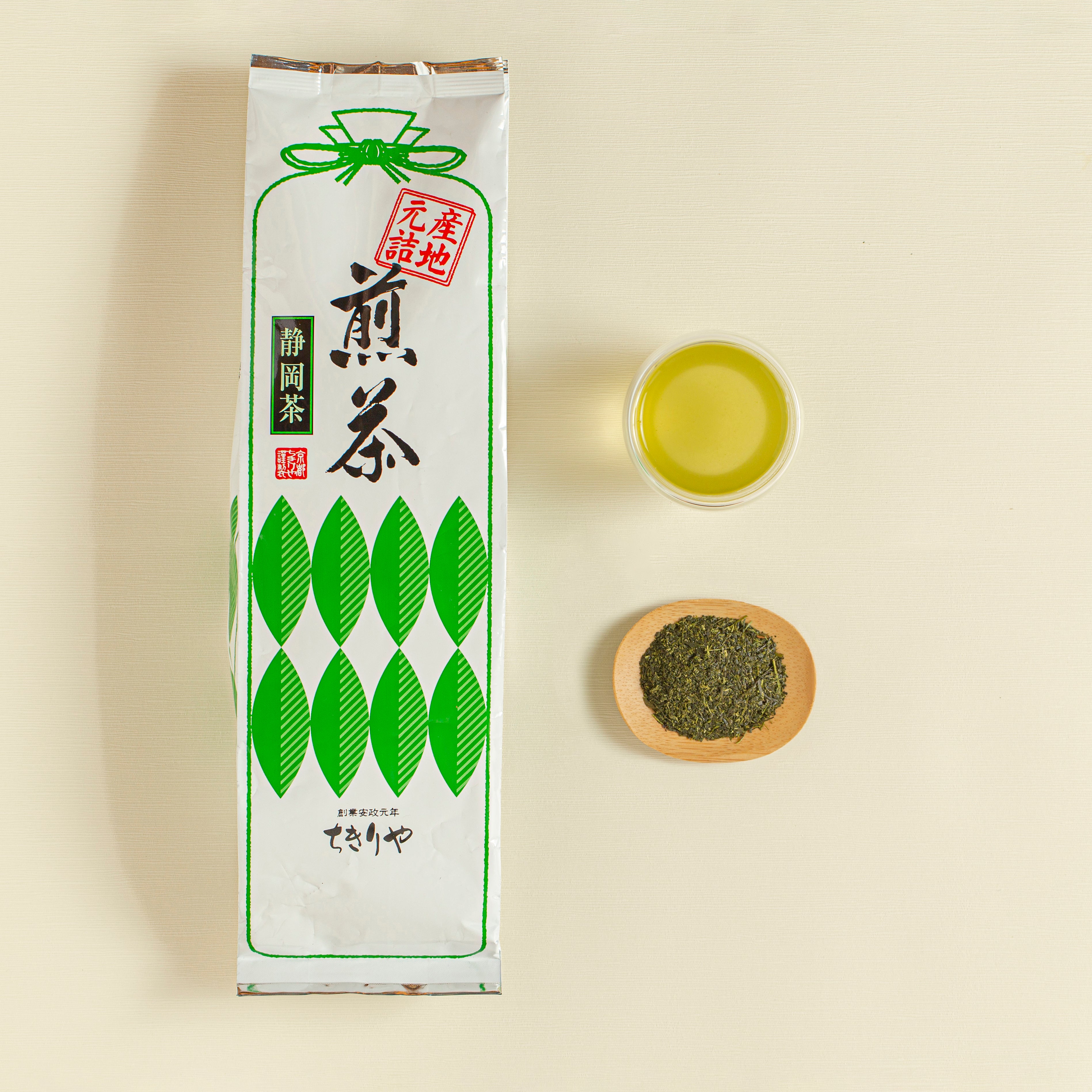 Tea package with a bowl of green tea leaves and a small cup of green tea on a beige background