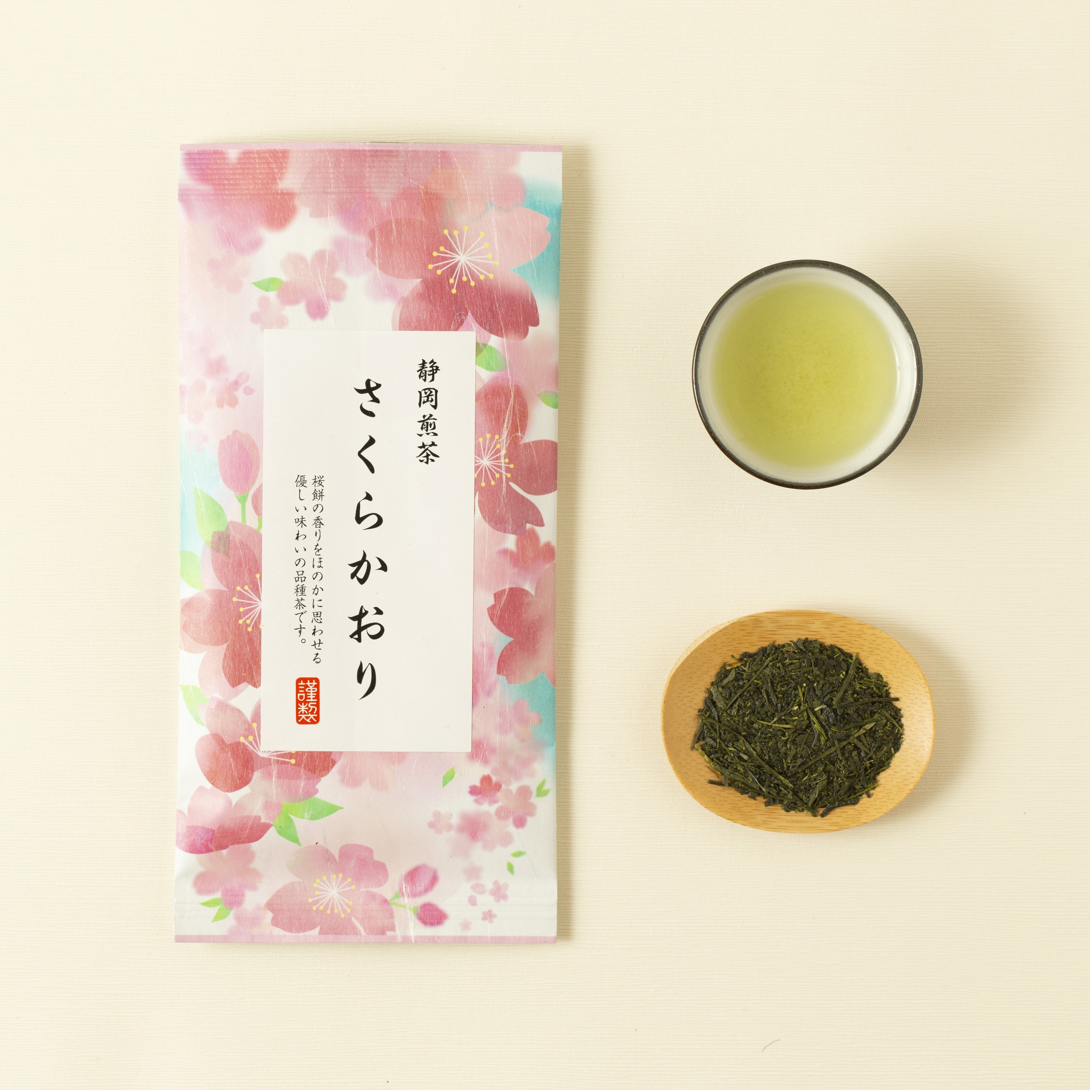 Tea package with cherry blossoms, a cup of green tea, and a bowl of green tea leaves on a beige background