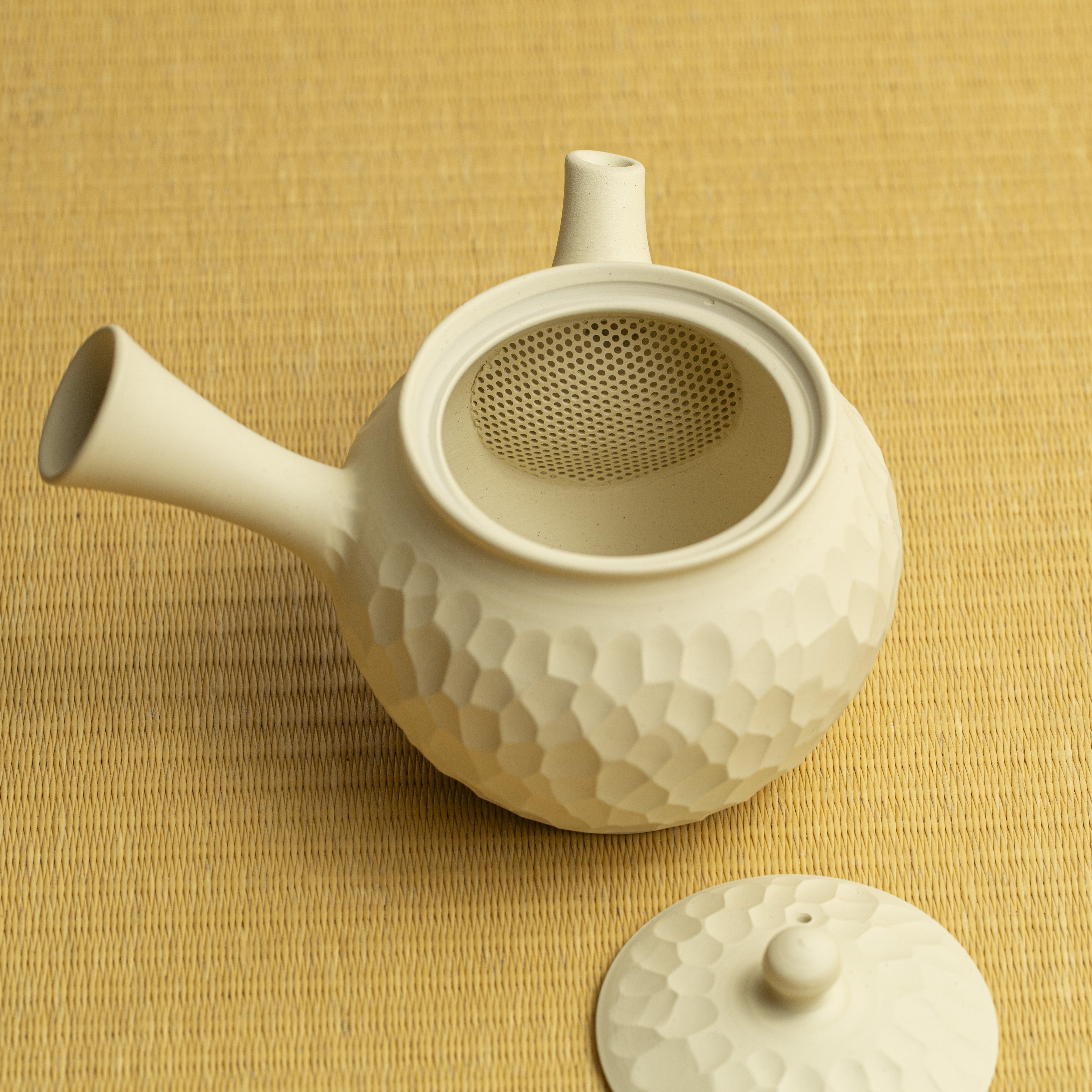 White ceramic teapot with textured surface on a yellow woven background