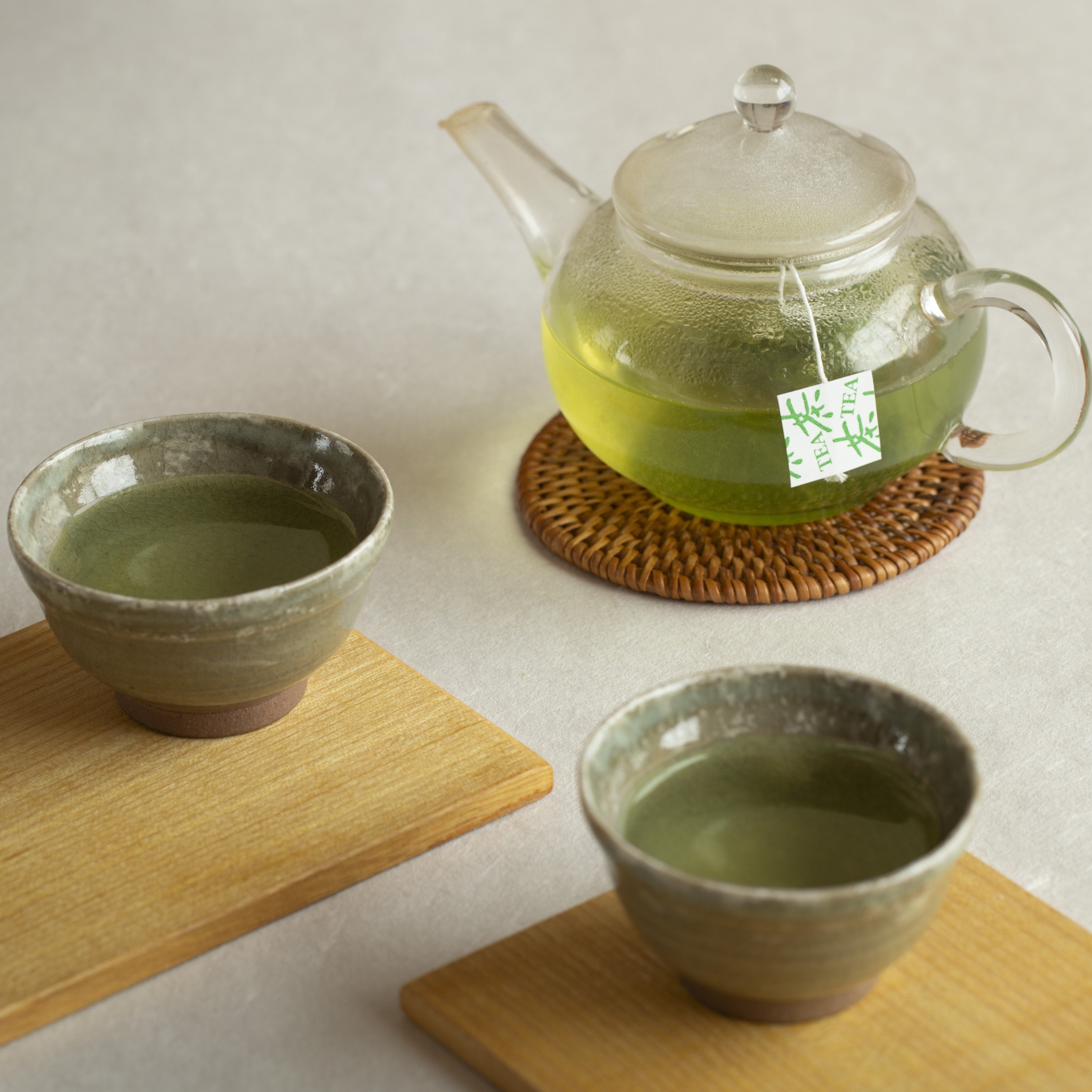 Tea set with a glass teapot and two ceramic cups on a light surface.