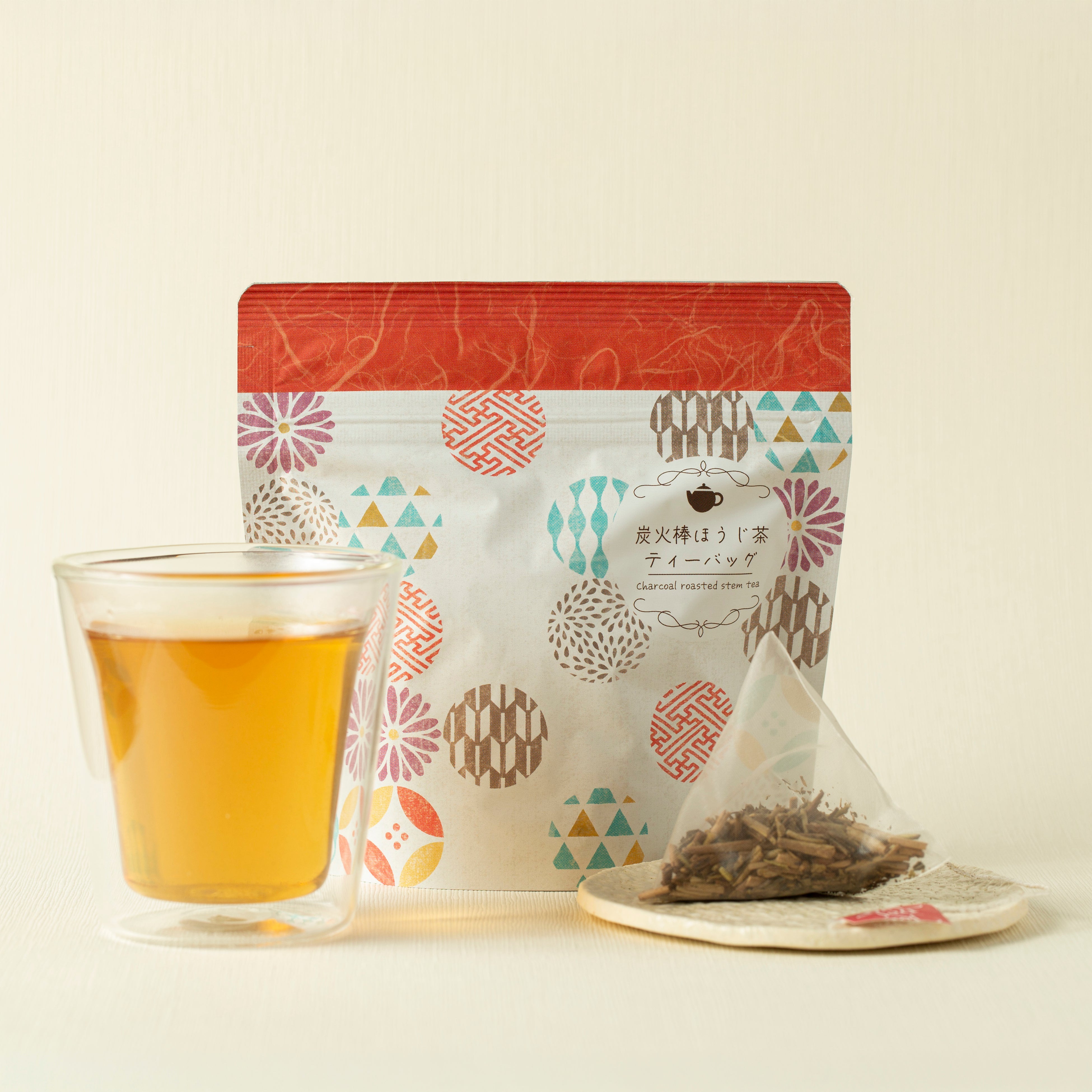 Tea bag with patterned packaging, glass of tea, and loose tea on a light background