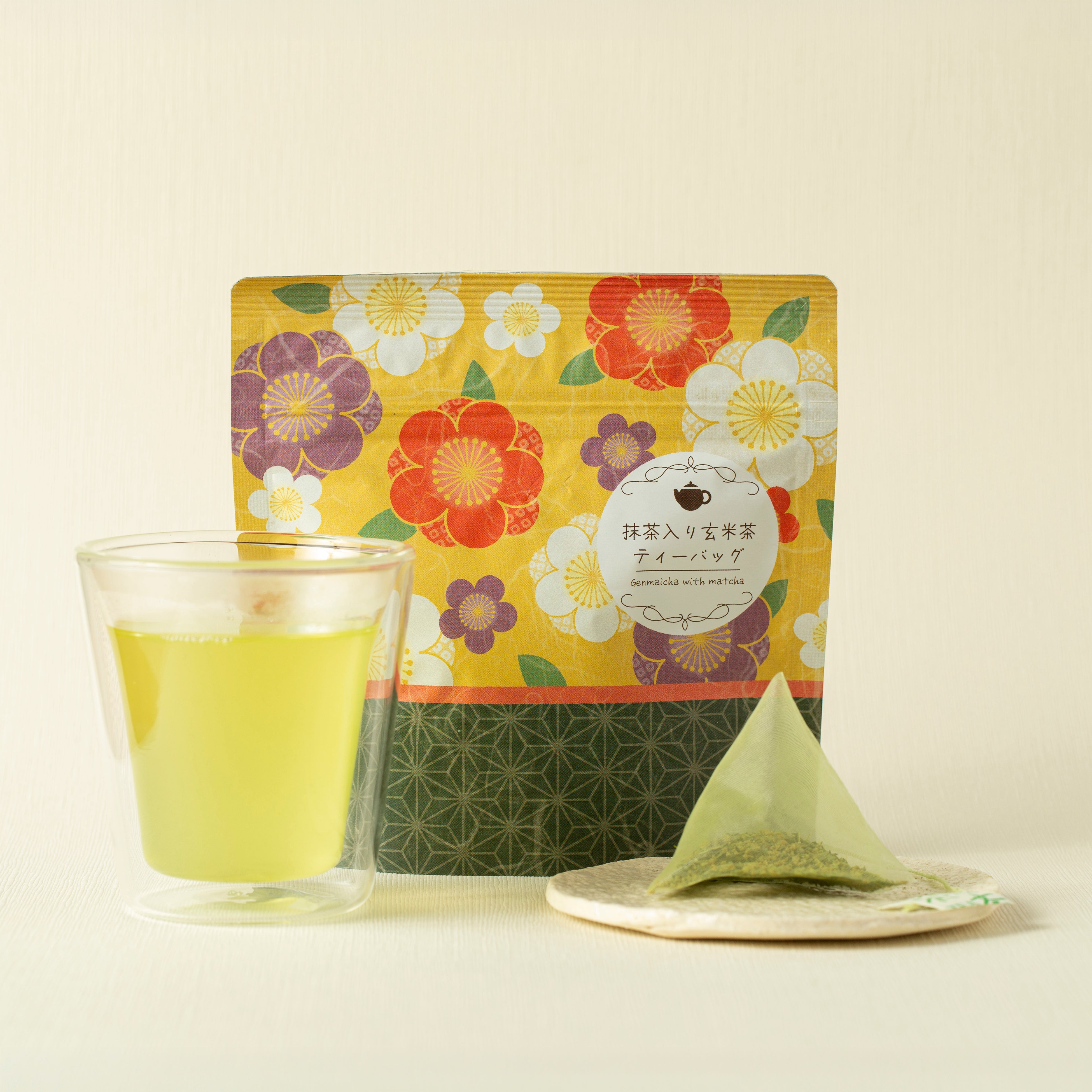 Tea package with floral design, glass of green tea, and tea bag on a light background
