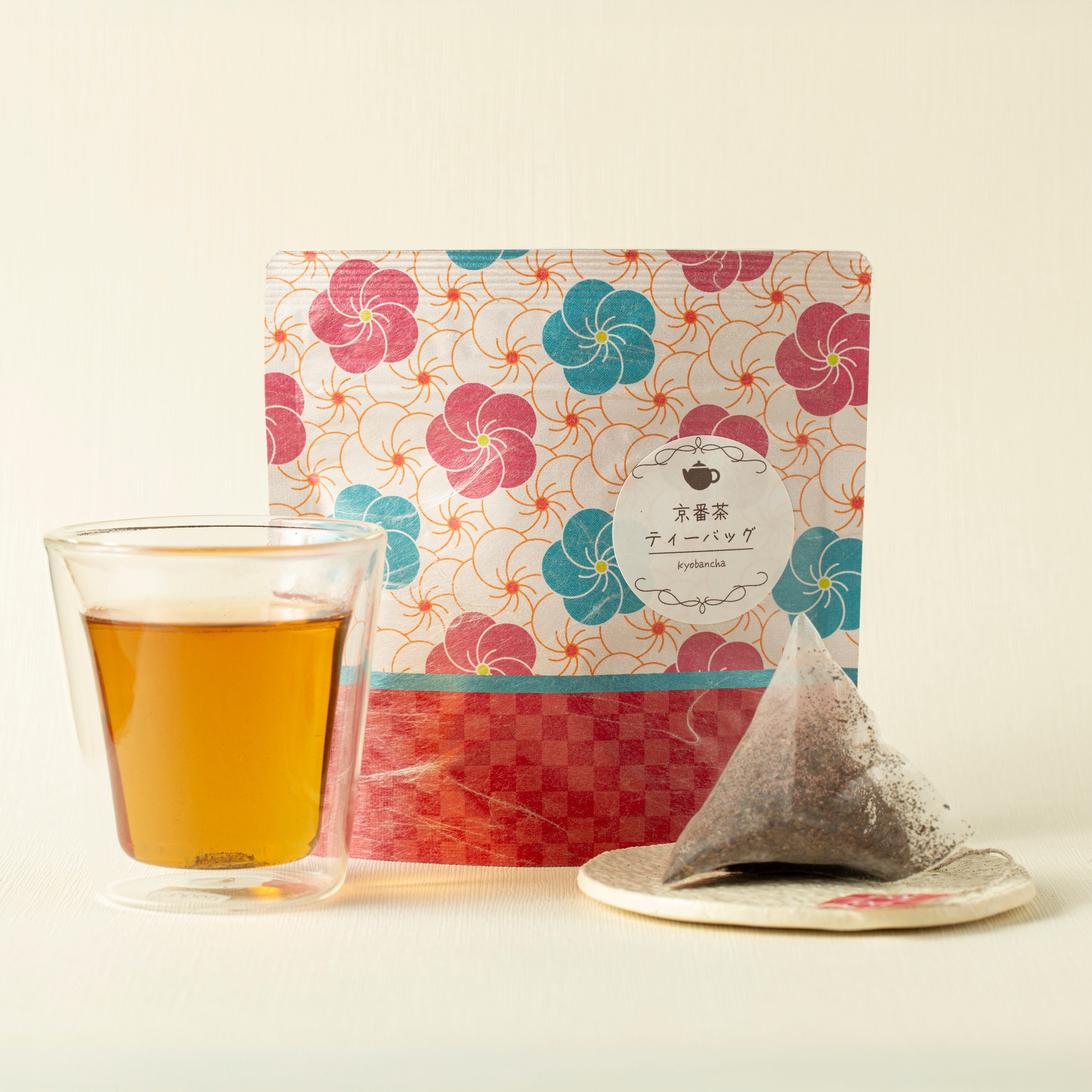 Tea bag package with a floral design, a glass of tea, and a tea bag on a light background