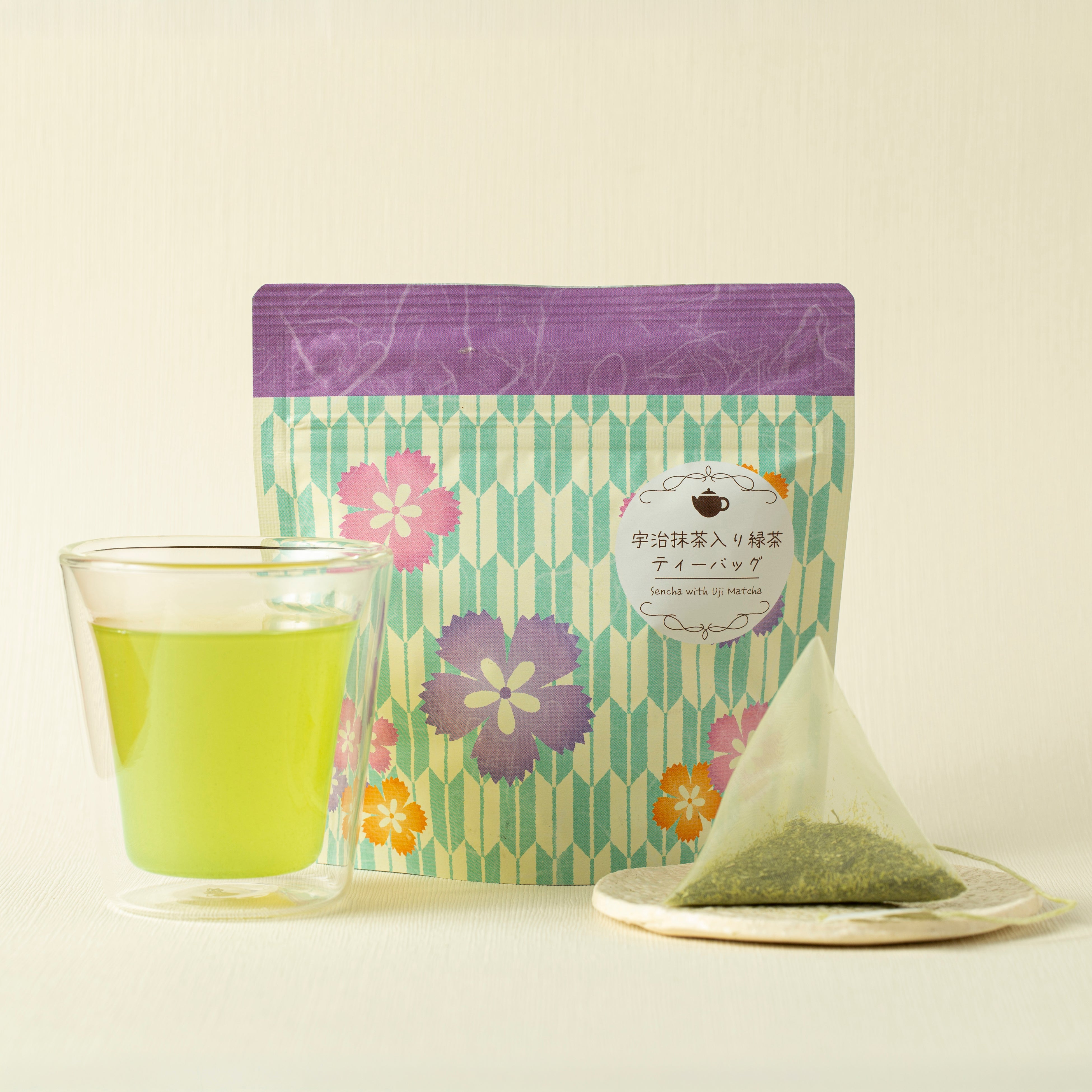 Tea package with floral design, glass of green tea, and tea bag on a light background