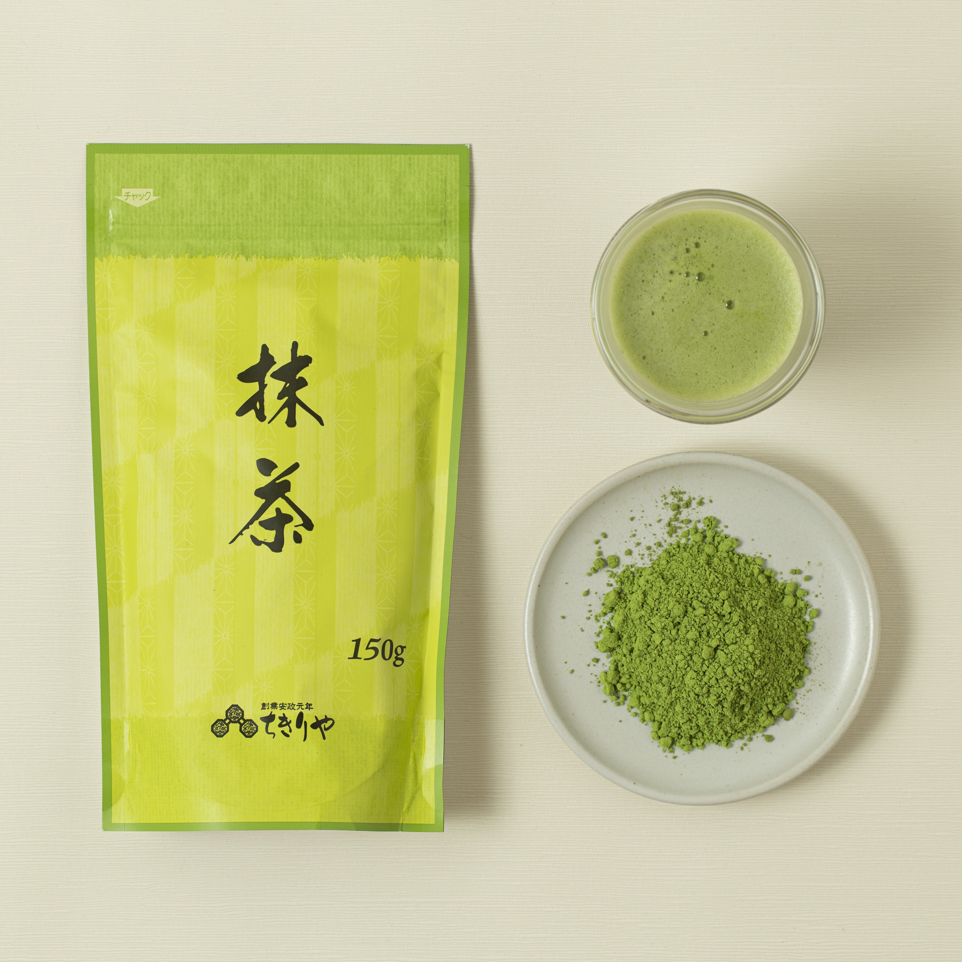 Matcha green tea packaging, bowl of matcha powder, and cup of matcha on a beige background